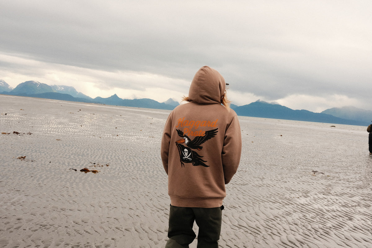 Big Beak Midweight Pigment Hoodie - Washed Clay — back view worn on an Alaska beach